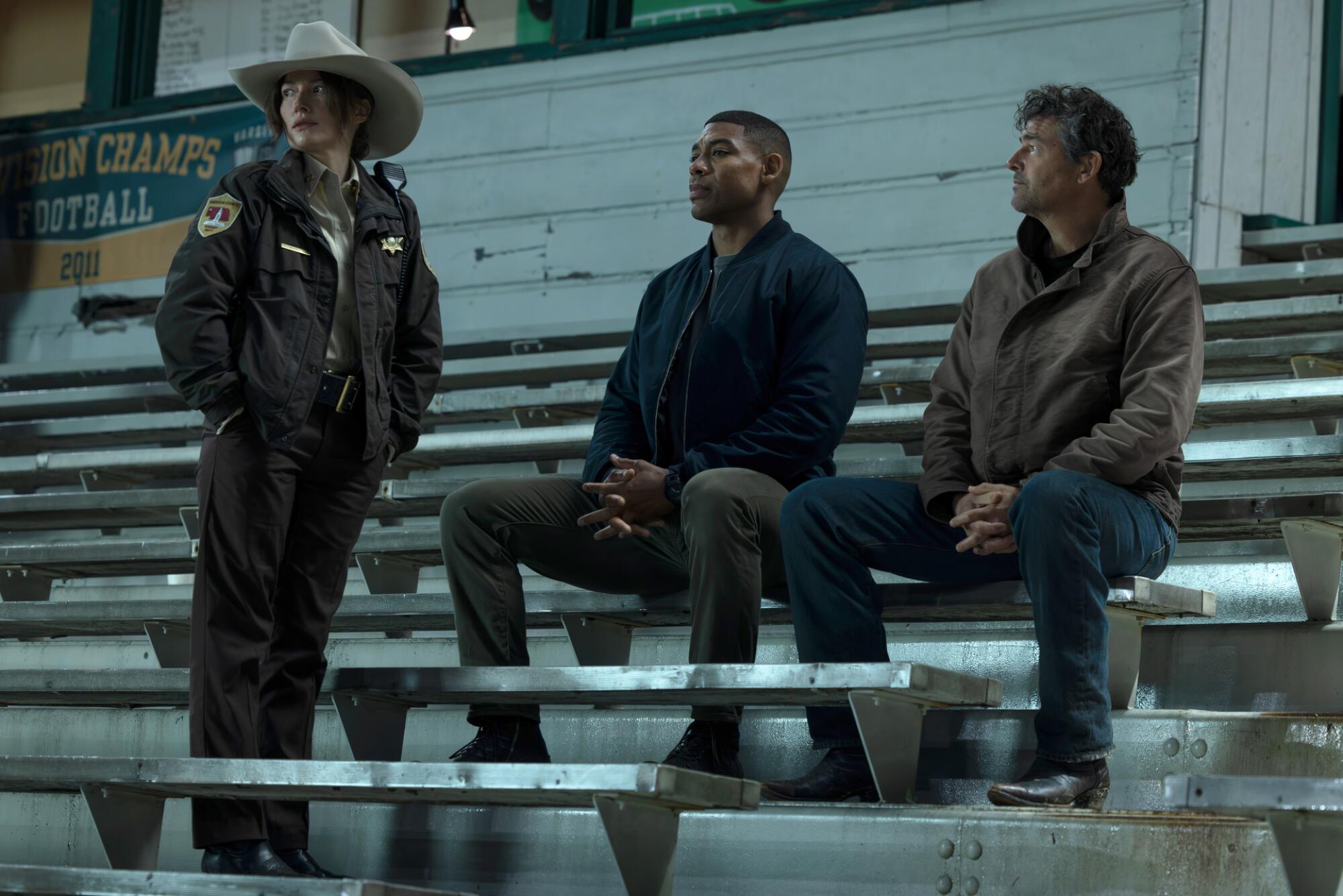 a sheriff stands in front of two men sitting in football stands
