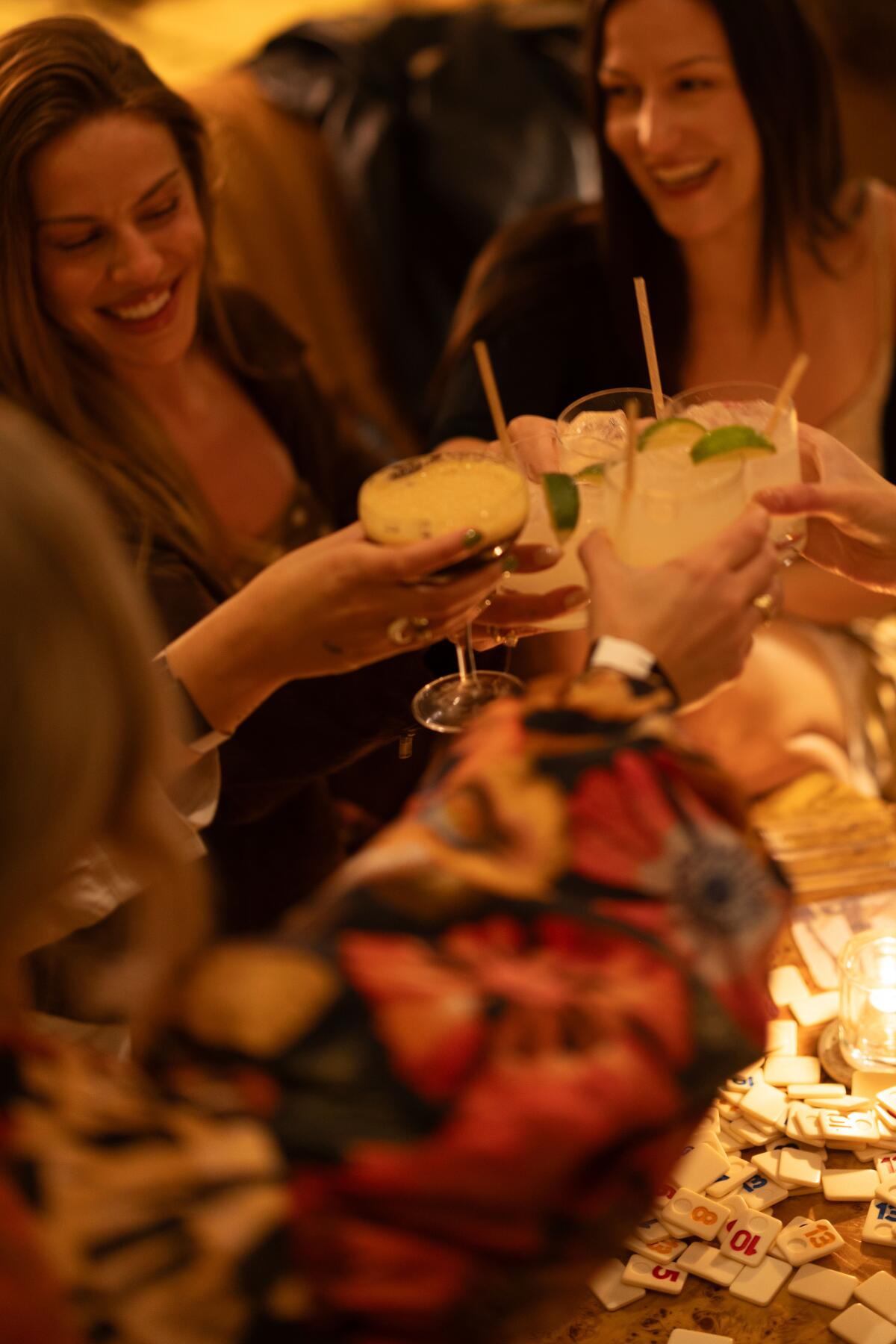 Three women cheers with cocktails at a table.