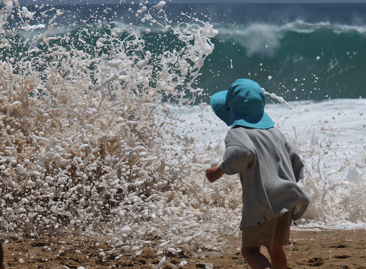 A youngster on the beach at the Wedge in Newport Beach is sprayed by ocean water.