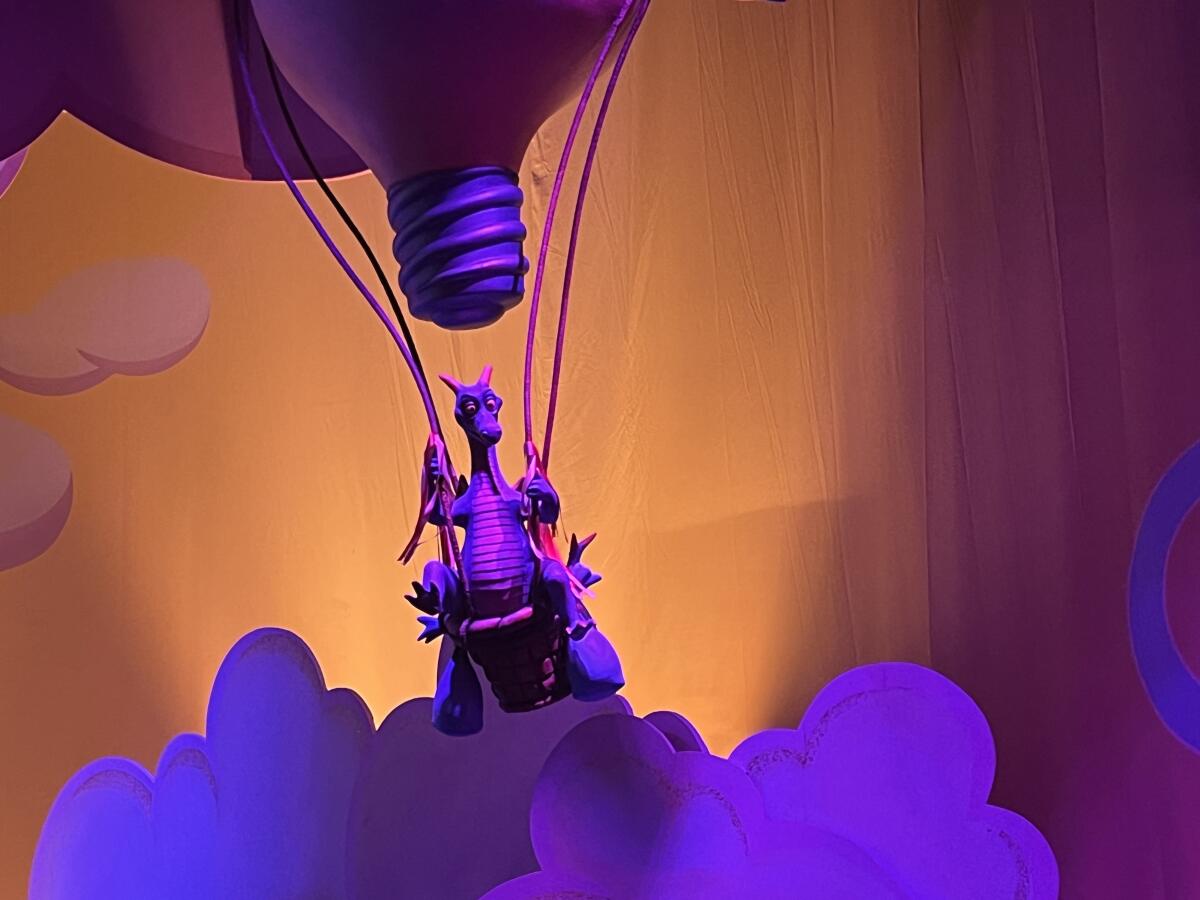 A purple dragon in a hot air balloon that looks like a lightbulb in a theme park ride. 