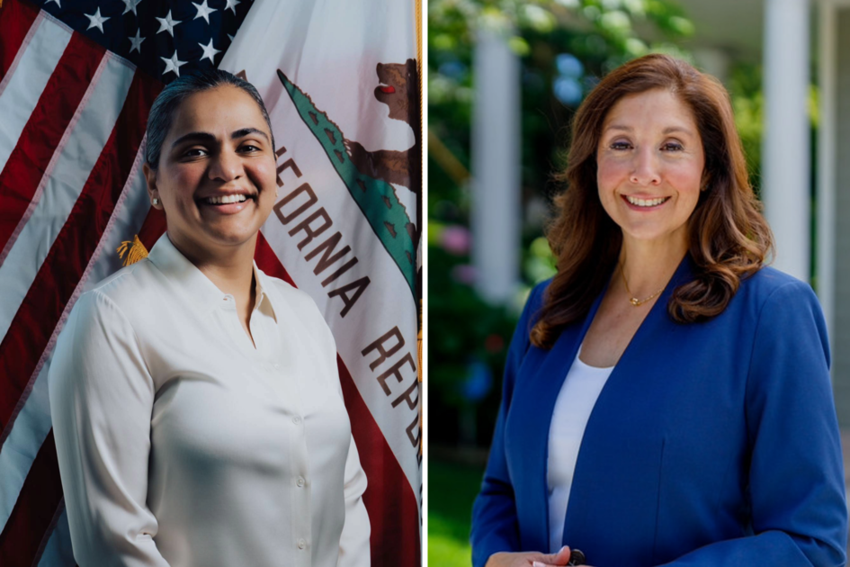A woman in a white blouse stands smiling in front of U.S. and California flags, next to a woman with brown hair wearing a blue blazer and white top outdoors.