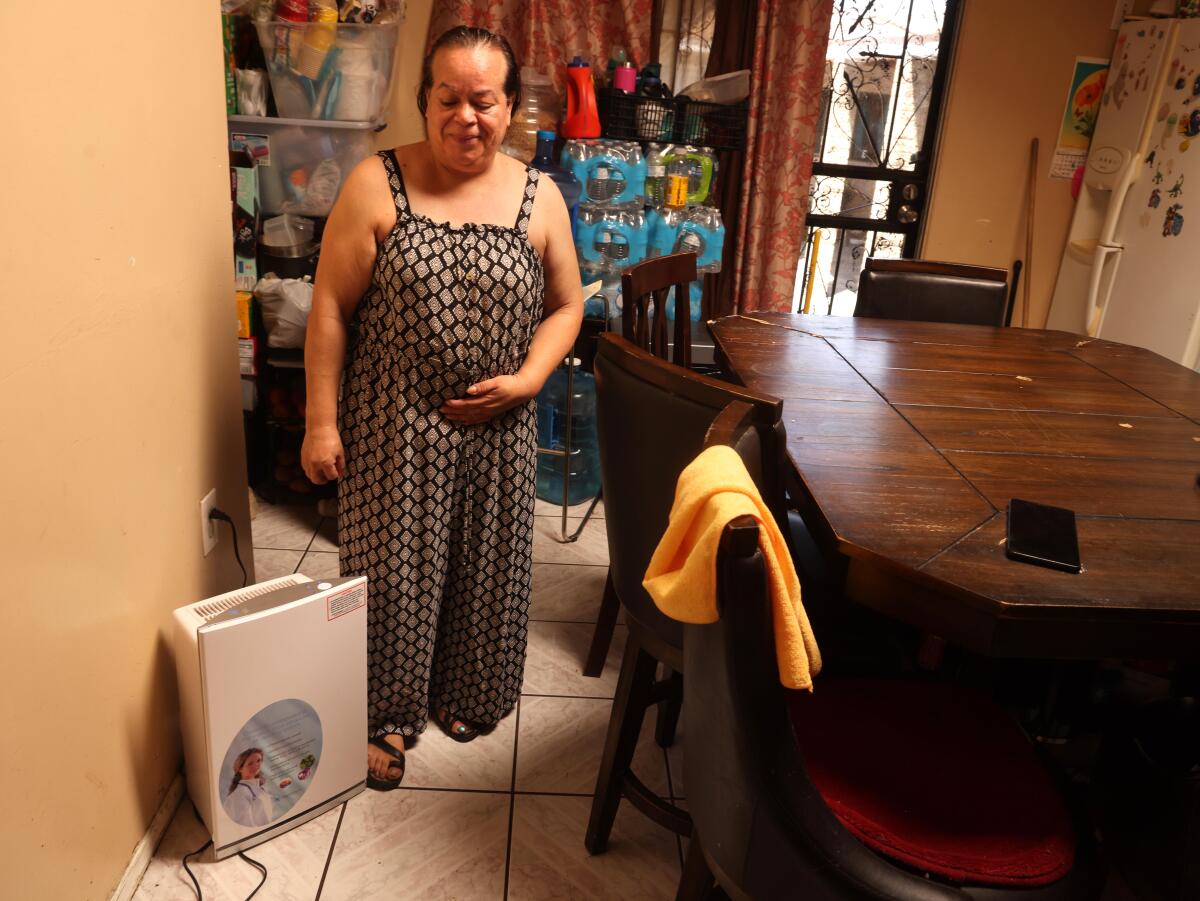 a woman stands next to an air purifier in the kitchen of a home.