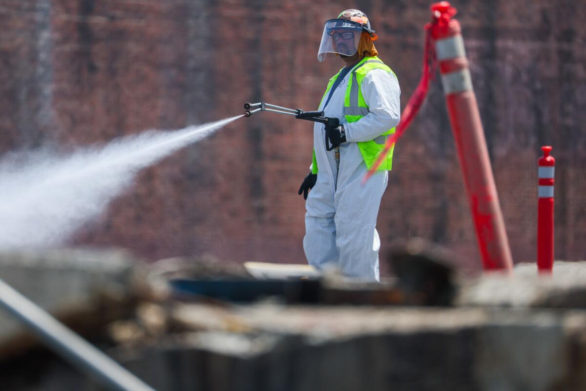 A person in a helmet-mask and full-body covering sprays water. 