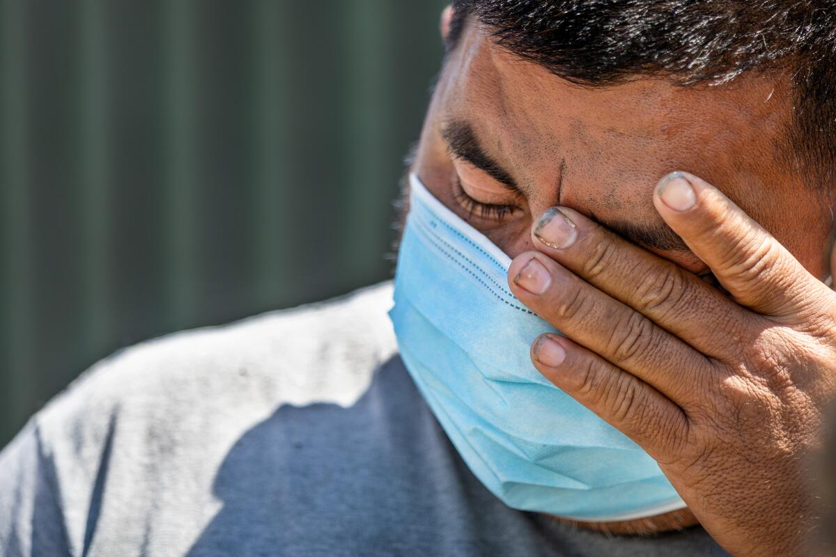 A person wearing a blue mask holds his hand up to his face.