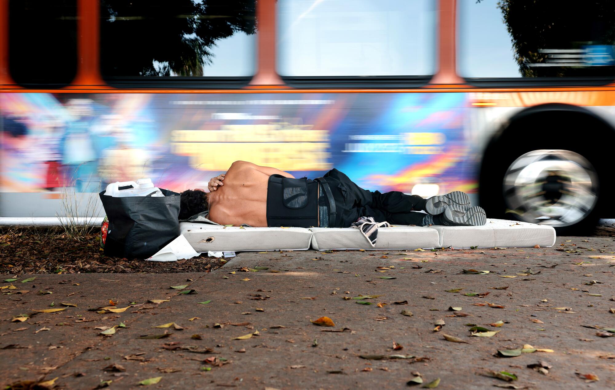 A Metro bus passes by a man sleeping on the sidewalk.