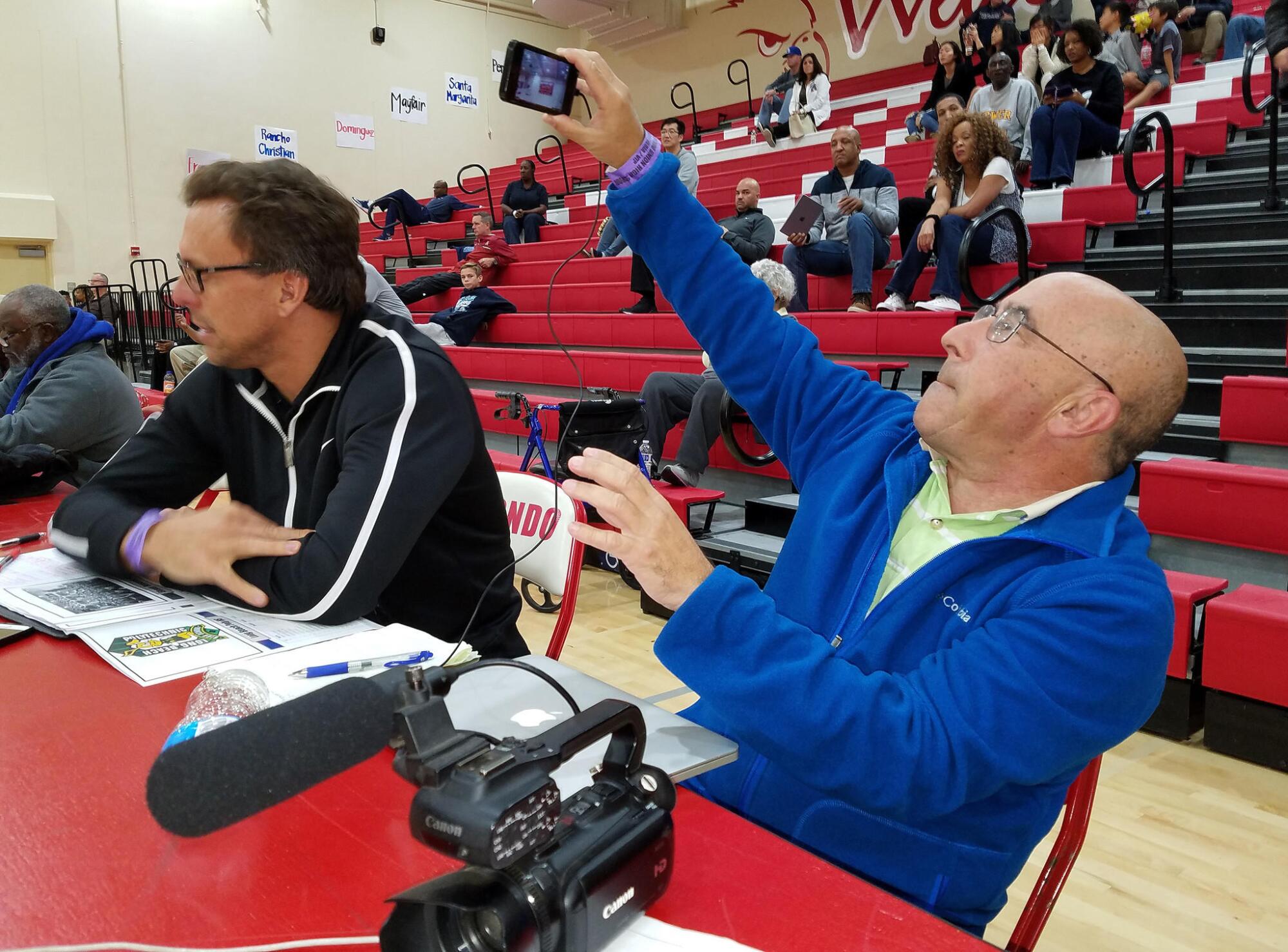 Eric Sondheimer shoots a video with his cellphone from the scorer's table while covering a basketball game.