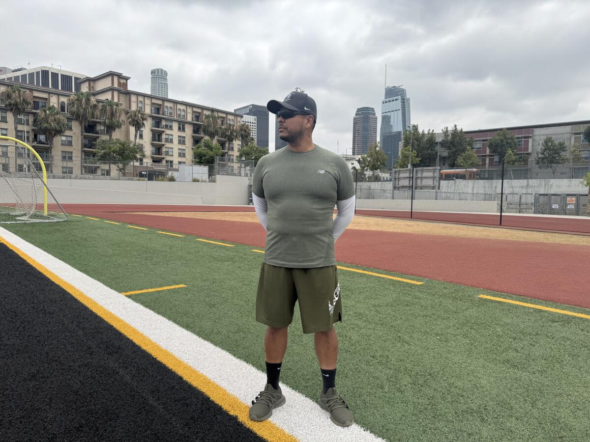 With downtown in the background, Contreras football coach Manuel Guevara stands on his school's field.