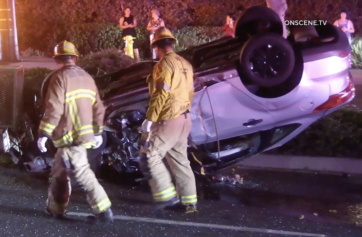 Firefighters pass a vehicle on its roof 