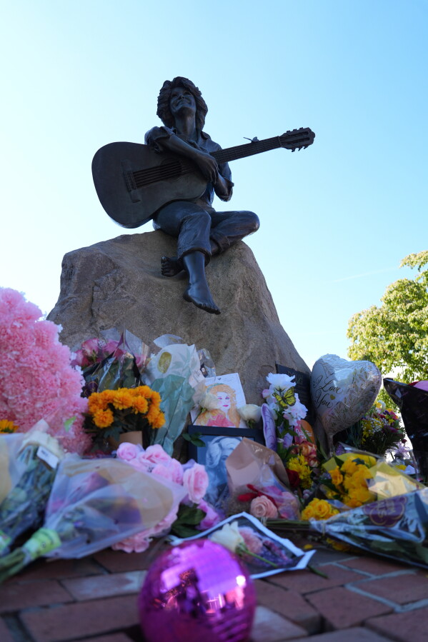 Flowers surround a statue of Dolly Parton in Sevierville, Tenn., Tuesday, Aug. 25, 2026. (AP Photo/Camden Hall)