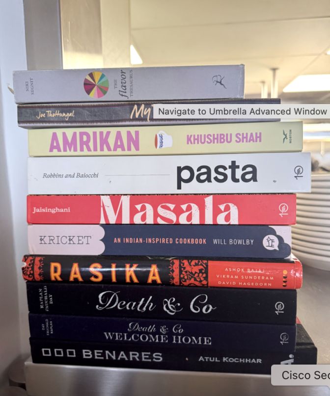 A pile of colorful cookbooks are lined up on a metal shelf.