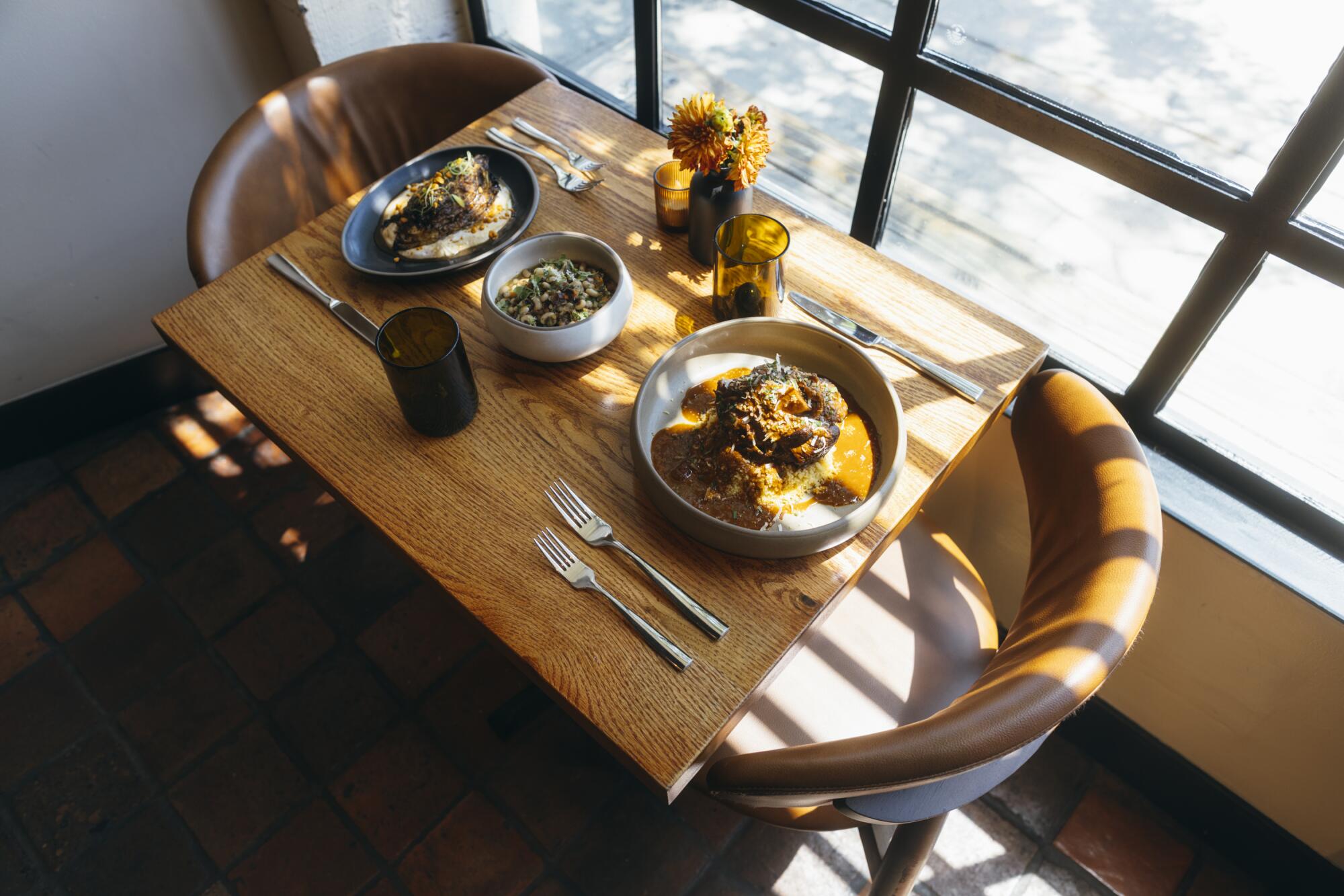 A windowside table at Alta Adams restaurant in West Adams with dishes such as roasted cabbage and black-eyed pea salaad.