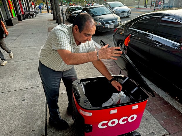 Bobby Saini, owner of Punjab Cafe on E Santa Clara Street, places an order of butter chicken and spicy garlic naan in a Coco delivery robot on Tuesday Aug. 11, around dinnertime. He says the robots showed up to pick up orders a couple of months ago, sometimes picking up four to five deliveries a day, "sometimes more on weekends." (Ryan Macasero/Bay Area News Group)