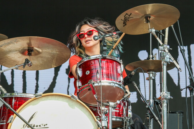 A drummer wearing red sunglasses and dyed hair beats cymbals.