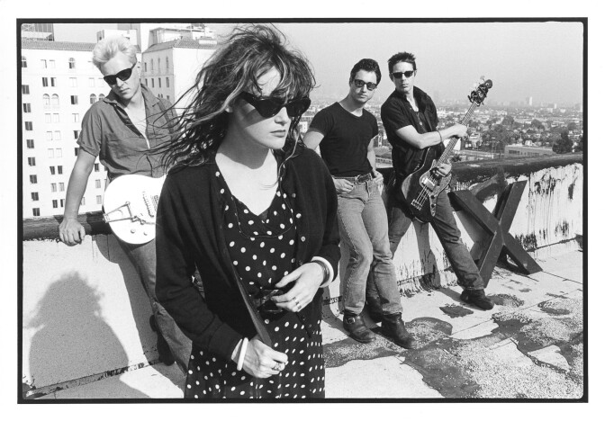 A woman in sunglasses and three men behind her -- two of them with guitars -- on a rooftop overlooking downtown L.A.