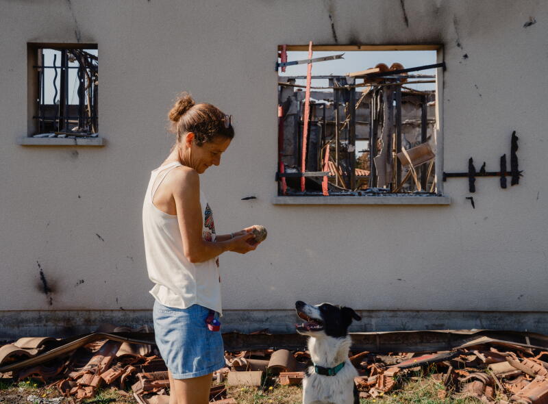 a woman and her dog interact in front of a burned out home