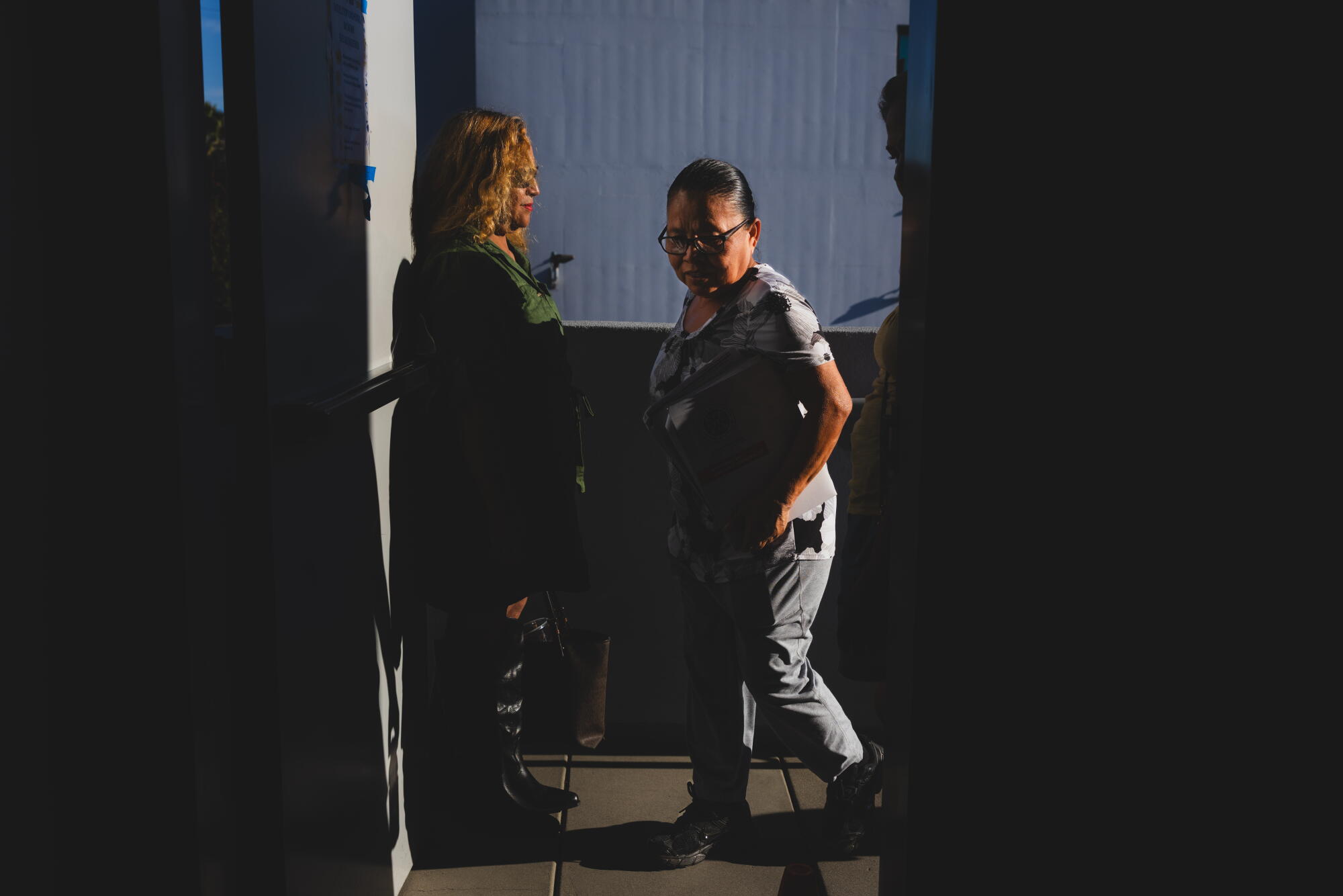 A woman walks through a doorway inside a dark room.