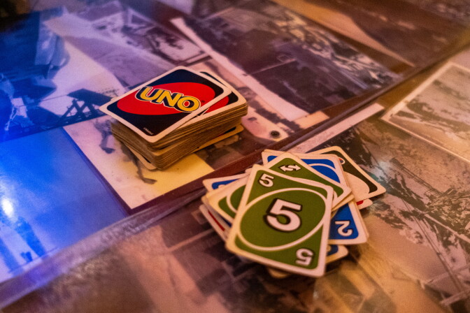 A deck of Uno cards sits beside a played hand of number cards, on a table with black-and-white photographs underneath.