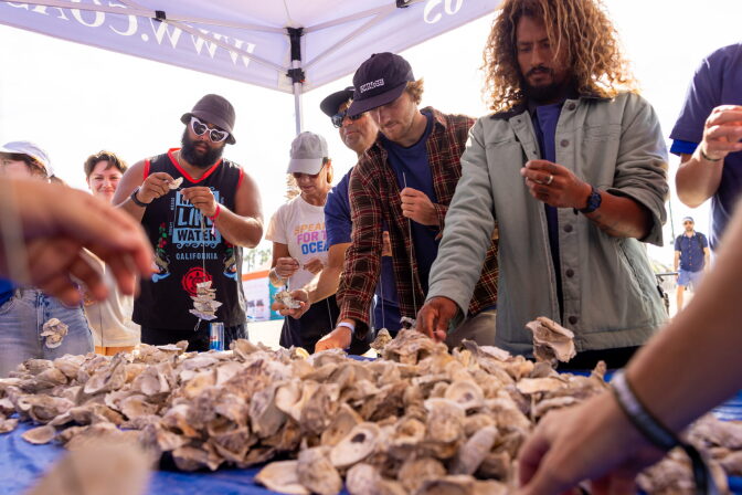 A group of five people stand around a table covered in live oysters.