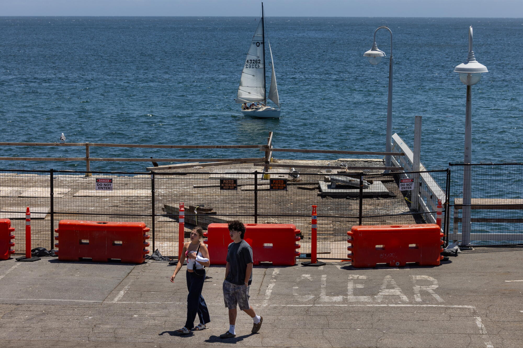people walk past a pier and sailboat