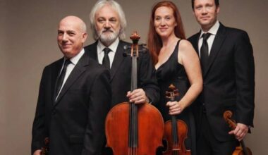 three male and one female string players in concert attire hold instruments