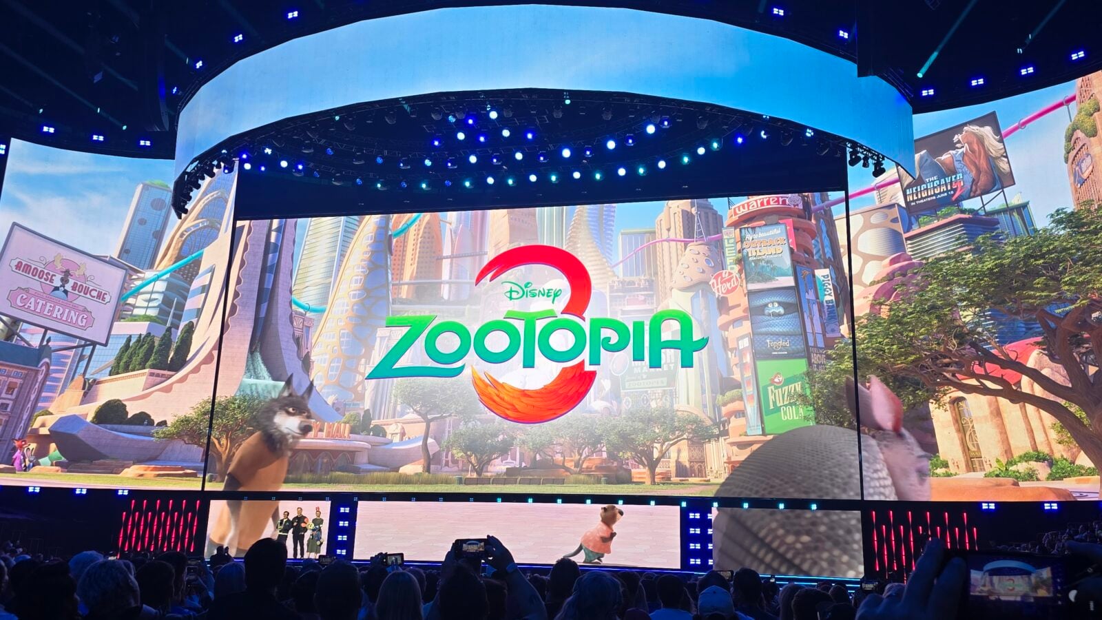 Large stage with a curved LED screen showing Disneys Zootopia branding and colorful cityscape audience watching a live event
