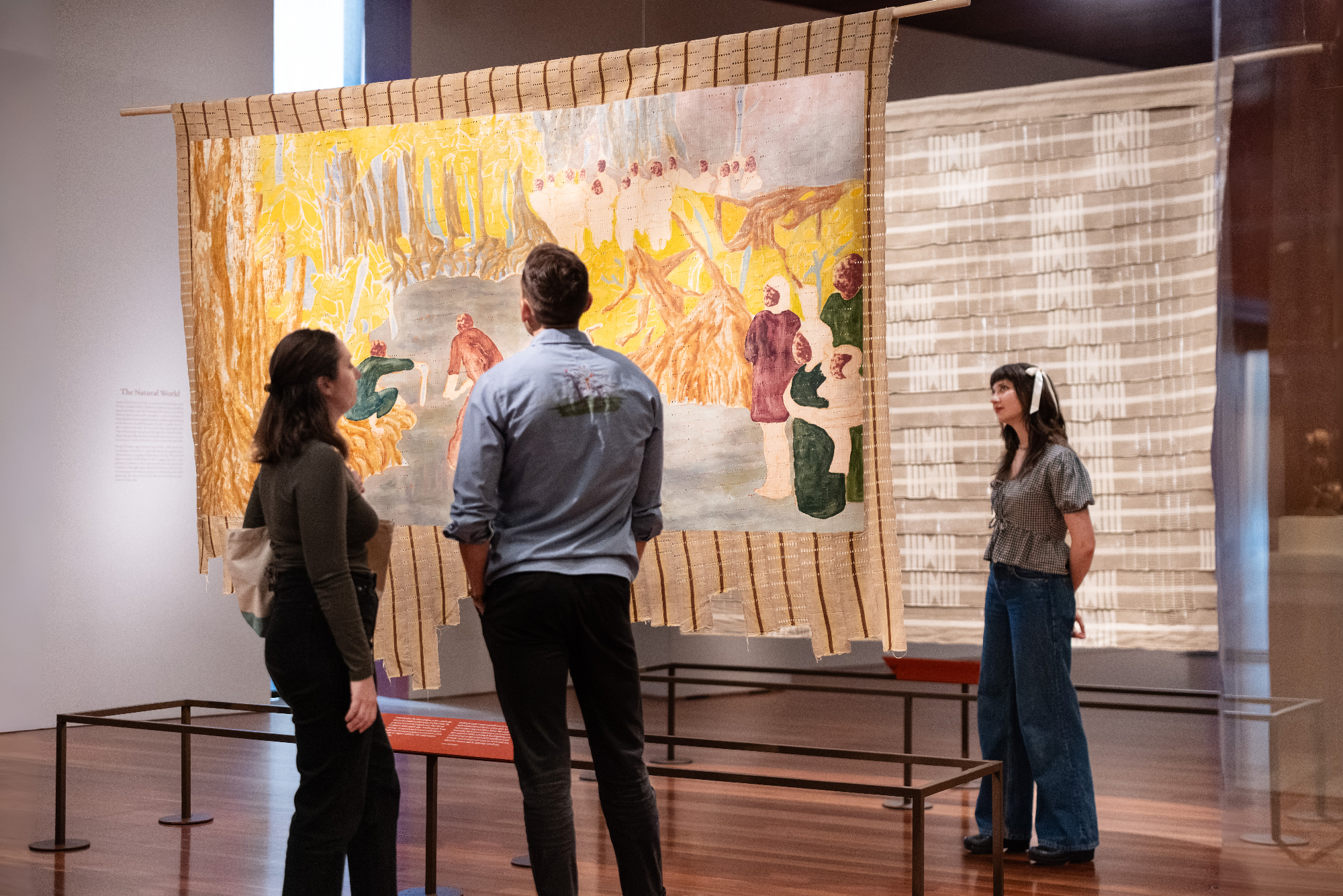 people stand in museum gallery looking at backs and fronts of suspended paintings