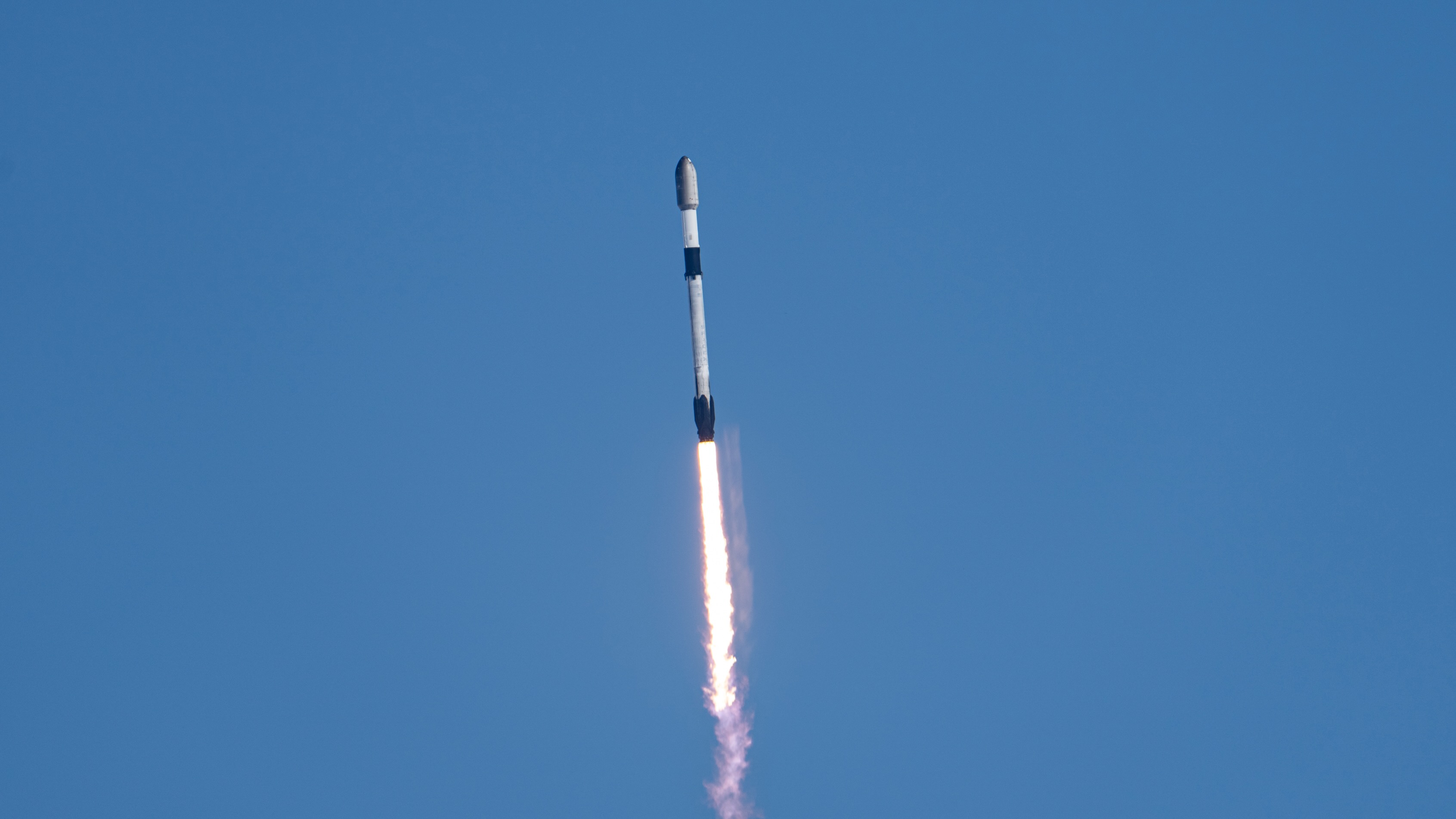 a black-and-white spacex falcon 9 rocket launches into a blue sky.