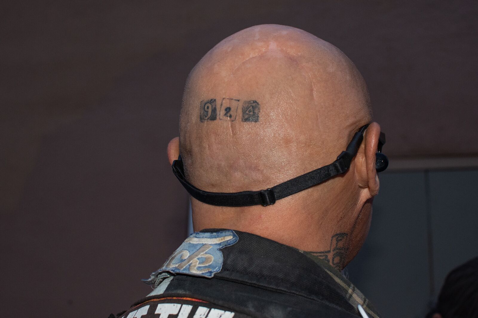 The back of a man's shaved head has a tattoo that reads "924"