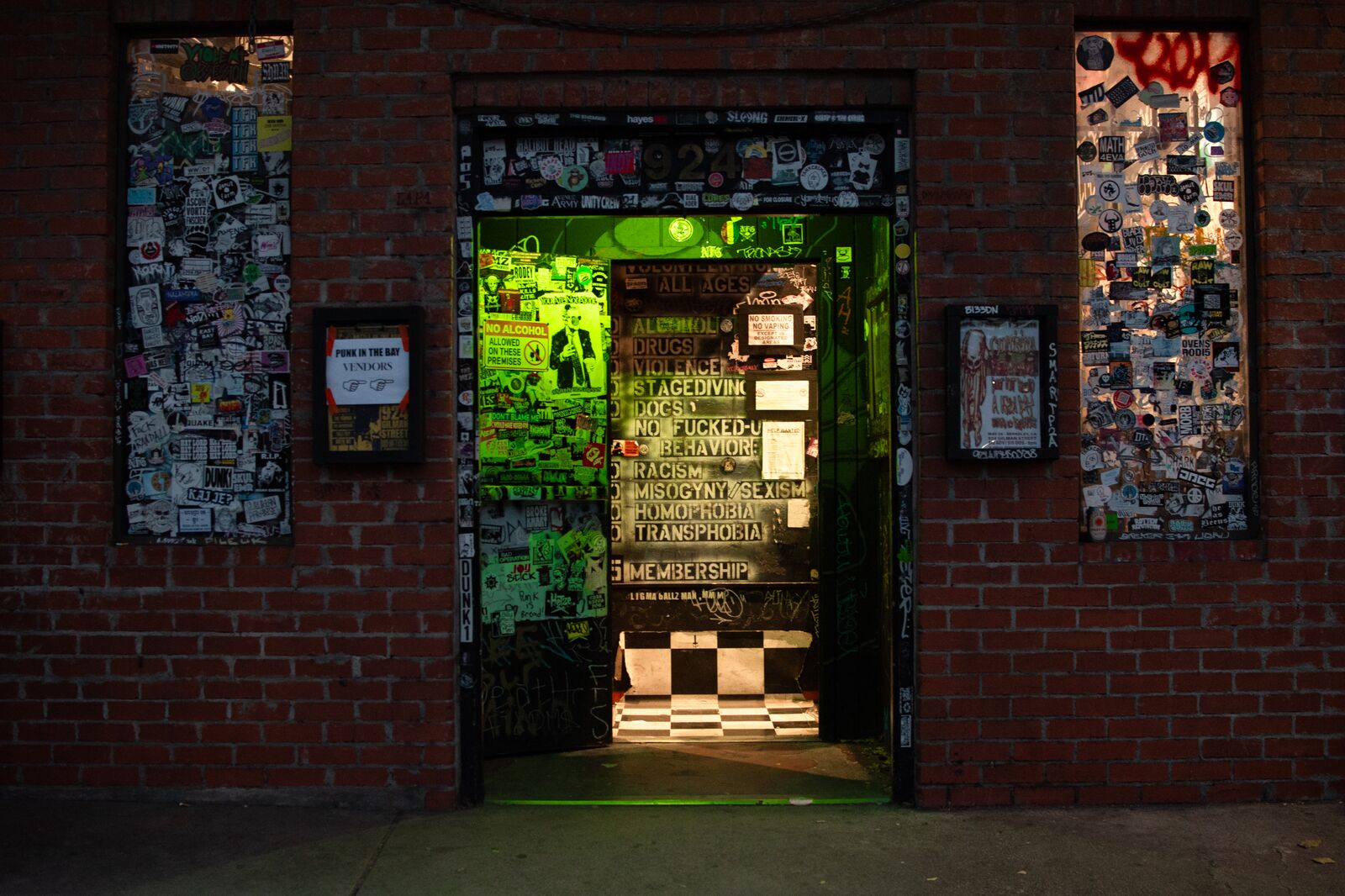 A view of the entryway to 924 Gilman, where the exterior walls are covered in stickers and graffiti and the interior wall has a spray-painted list of rules