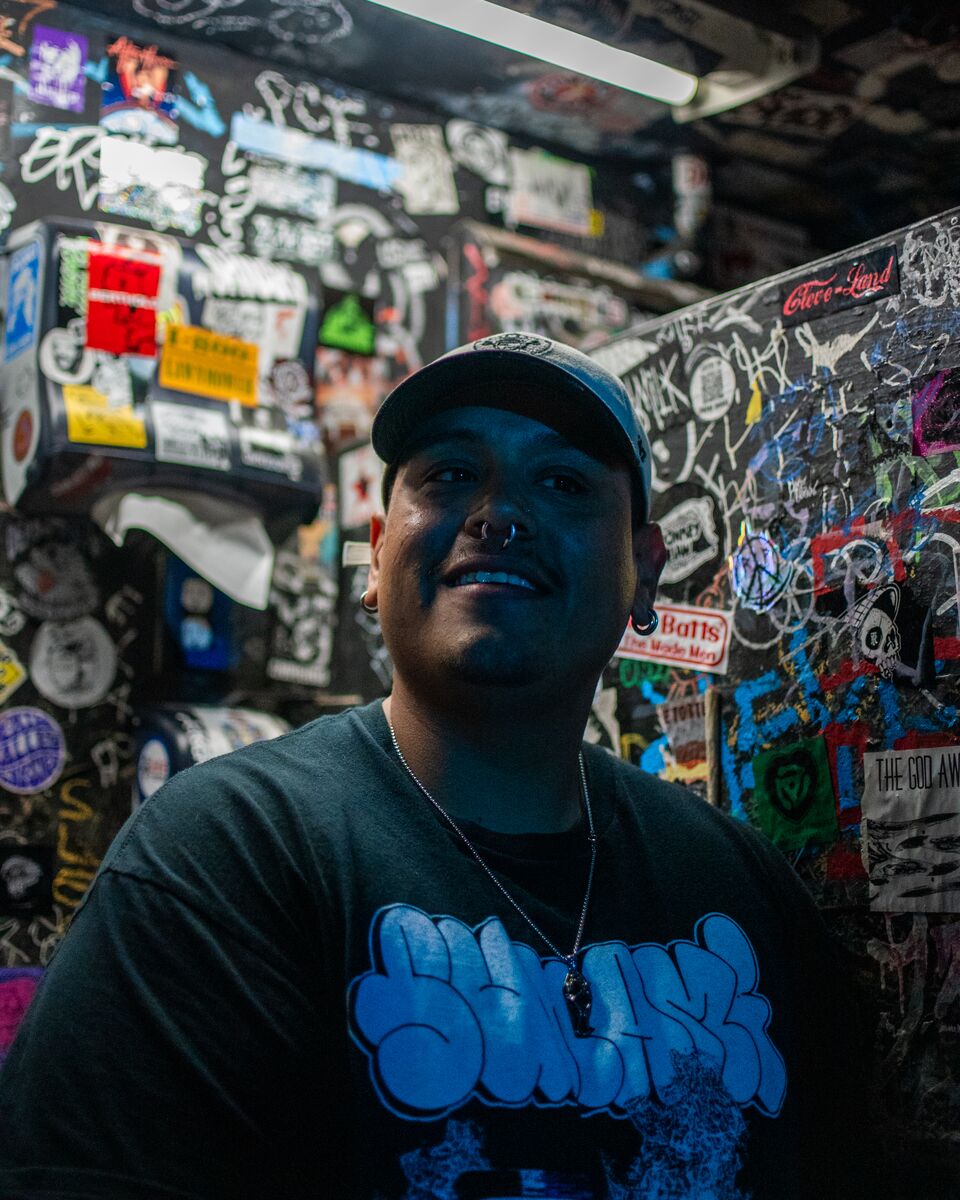 A man wearing a black graphic T-shirt poses for a photo inside a graffiti-covered bathroom