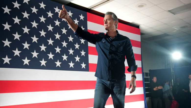 A person giving a thumbs-up standing in front on a large American flag display.