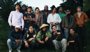 big group of musicians stand and crouch, slightly smiling