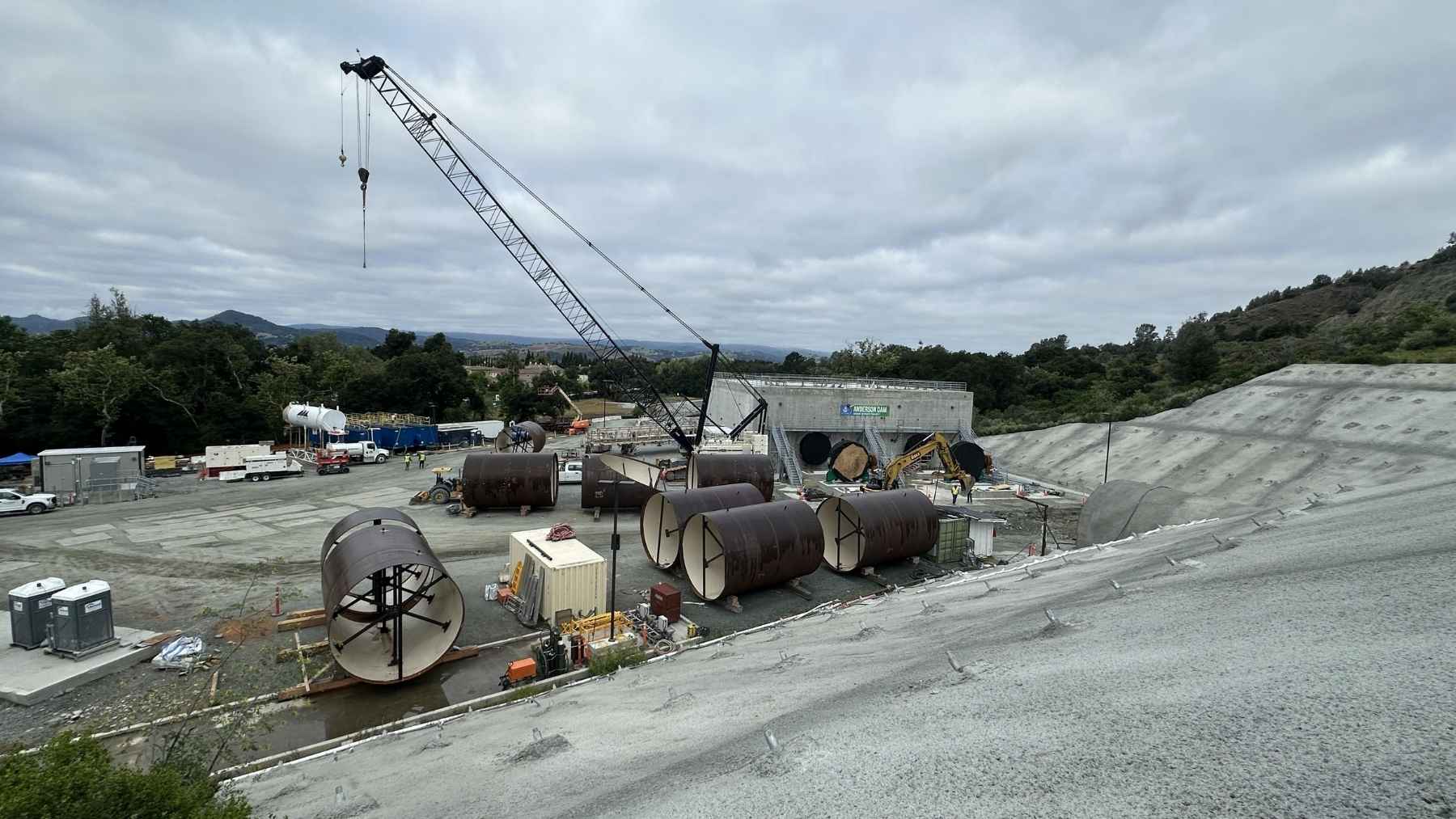 California just finished shoving an 8-foot boring machine 347 feet under a lake with nothing to brace against, coming out through the reservoir floor with the water still sitting on top, and the dam above it is now coming down for a rebuild