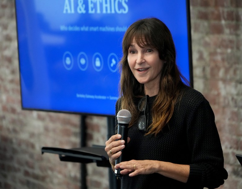 A person speaking into a microphone at an event titled "AI & ETHICS" in front of a blue screen.