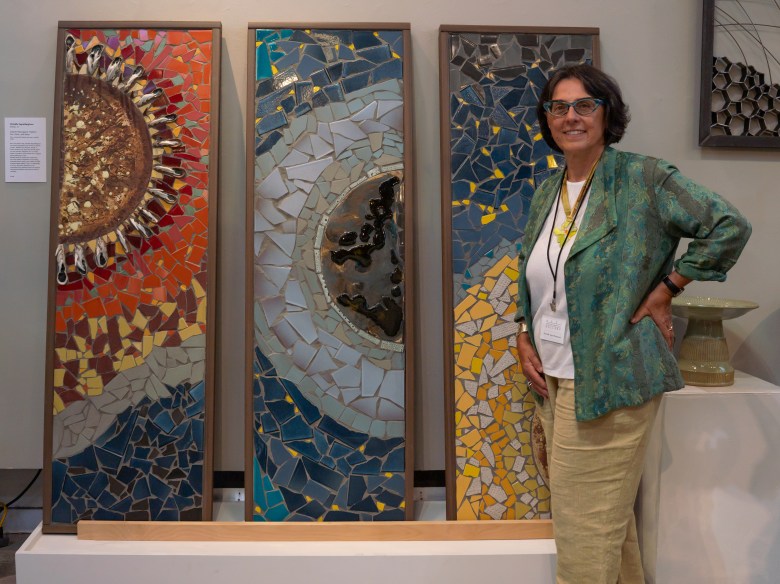 A person stands beside three vertical mosaic artworks featuring sun-like and wave-like designs, displayed on a white pedestal.