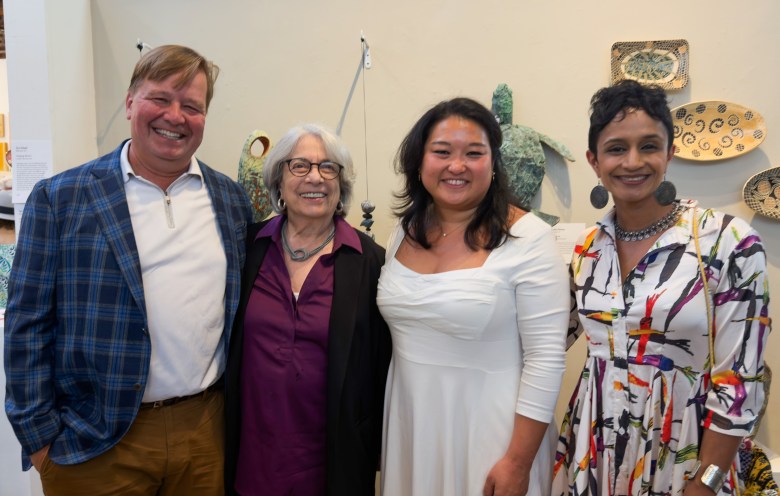 Four individuals smile for a photo in an art gallery setting, standing before various decorative sculptures and wall art.