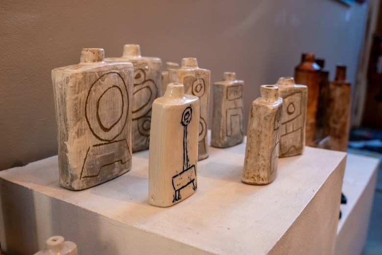 A collection of abstract ceramic vessels with hand-drawn geometric and symbolic markings displayed on a white pedestal.