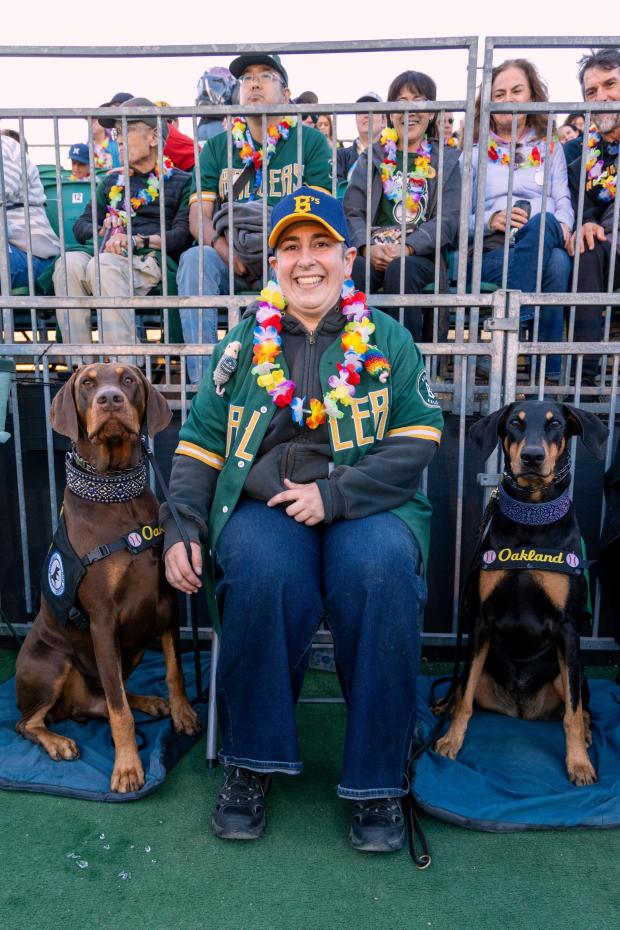 This photo provided by Darrell Lavin shows Colt Rosensweig and her service dogs, Curtis and Caris, attend an Oakland Ballers game on Friday, Aug. 28, 2026, at Raimondi Park in Oakland, Calif. (Darrell Lavin via AP)