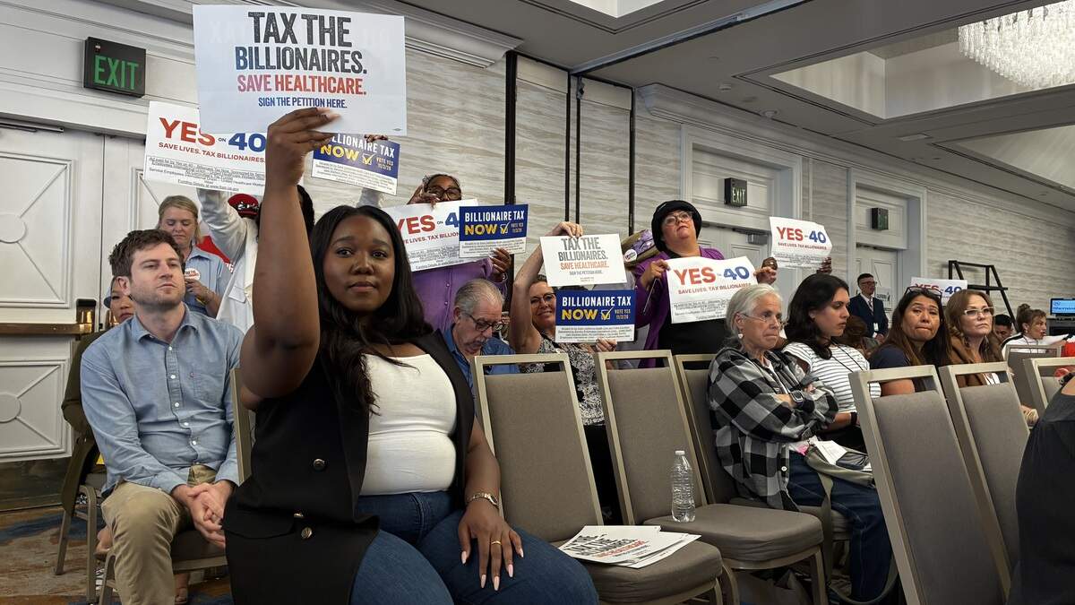 Supporters of the Proposition 40 billionaire wealth tax hold signs at a meeting of the California Democratic Party’s resolutions committee on Saturday, August 1, 2026 at the Sheraton San Diego Resort in San Diego, CA. Over a dozen supporters of the billionaire wealth tax hold signs in a conference room.