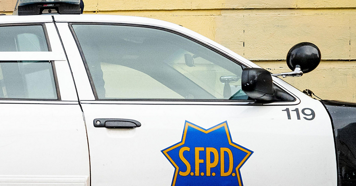 A white police car with the blue and gold emblem of "SFPD" on the side, marked with the number 119, parked against a yellow wall.