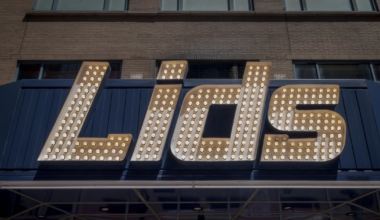 Large marquee lights spell out the word "Lids" on a dark blue sign mounted on a brick building.