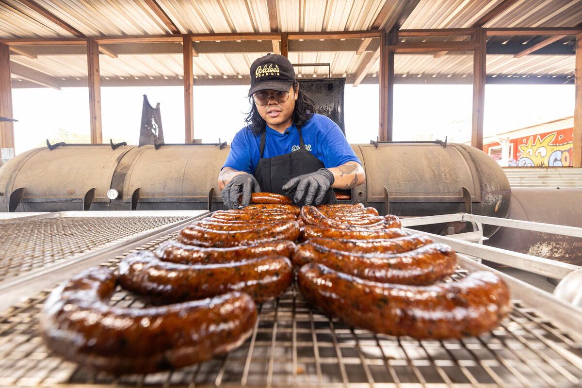 Nupohn Inthanousay, a co-owner of Goldee’s BBQ, takes Lao sausage out of the smoker and onto cooling racks before the Fort Worth restaurant opened for the day on June 28, 2024. “This is the food I grew up with and it’s a part of me,” he said. “A big part of me is being Lao, but also being Texan.”