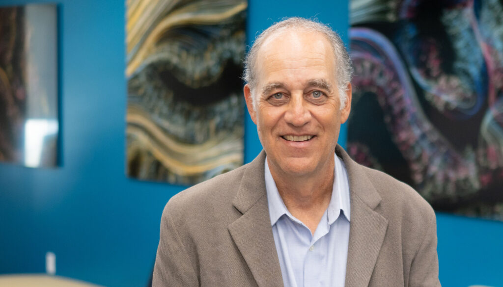 man in gray coat and blue shirt standing in front of colorful paintings