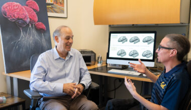 two men seated and talking in front of computer monitor with brains on the screen