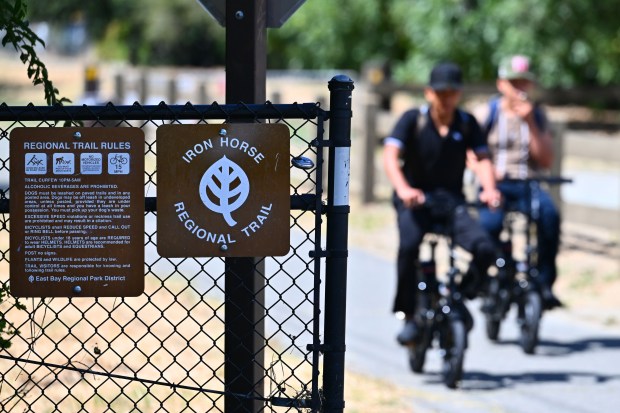 A pair of e-bike riders prepare to pass a posted sign on trail rules along the Iron Horse Trail in Pleasant Hill, Calif., on Thursday, July 2, 2026. The posted speed limit for bicycles is 15 mph. (Jose Carlos Fajardo/Bay Area News Group)