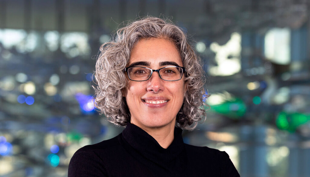 a woman in graying curly hair looking into the camera and smiling