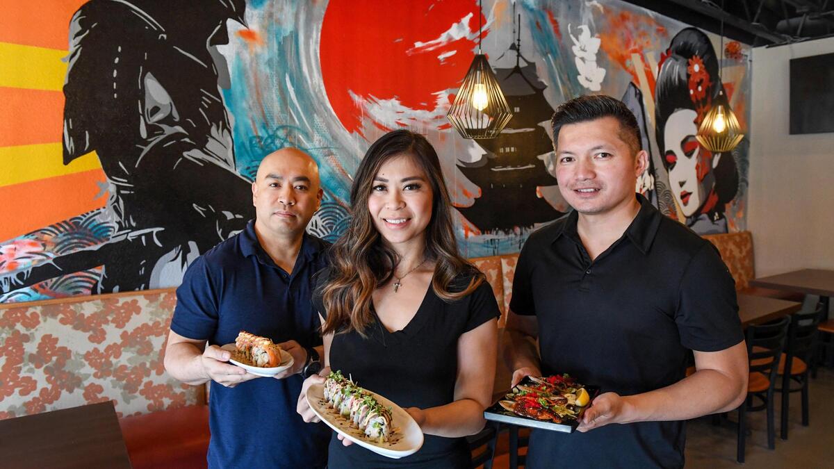 David Rasavong, right, who co-owns Banzai with his brother-in-law Westley Nguyen, left, and Rasavong’s wife Anna Nguyen, hold plates of food from the new Japanese restaurant in the Tower District when it opened in this file photo from March 26, 2021.