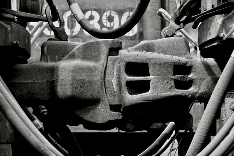 Close-up of an industrial metal machine component, surrounded by cables and hoses, in black and white.
