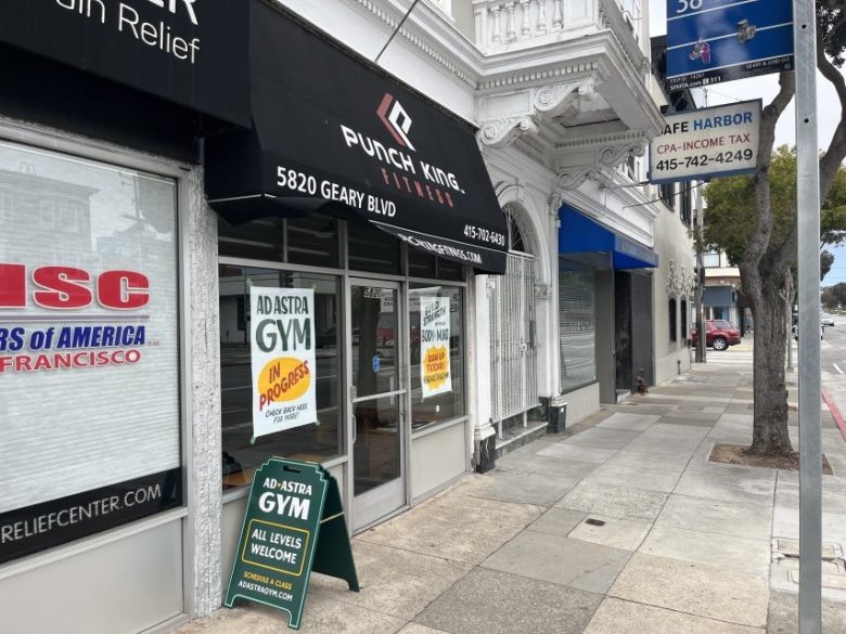 Storefronts on a city sidewalk include Punch King Fitness, Ad Astra Gym, and Safe Harbor CPA-Income Tax, with signs and a tree visible along the street.
