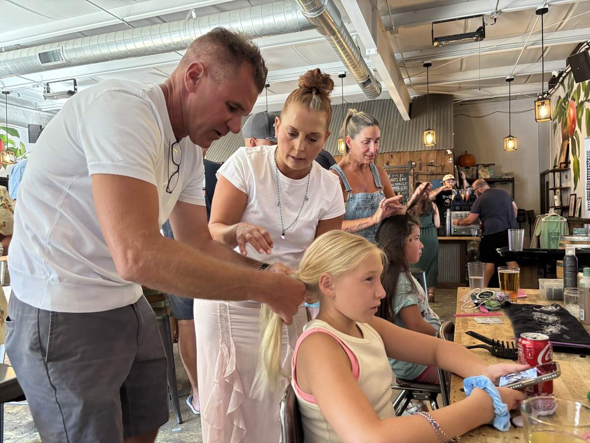 Strands Aveda hairstylist and manager Keri Crabtree teaches Justin Smith how to braid his 11-year-old daughter’s hair at the Pints and Ponies event at Nitty’s Cider in East Sacramento on Monday.